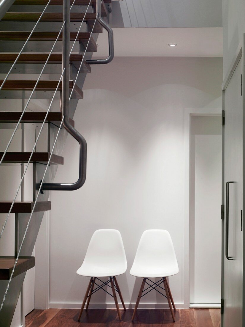 Retro chairs with white, plastic shell seats against wall in modern stairwell