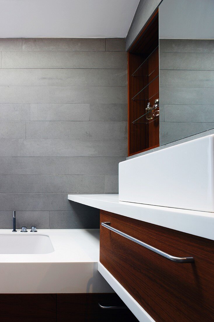 Ausschnitt eines grau gefliesten Designerbades mit Holzfront aus Nussbaum am Waschtisch