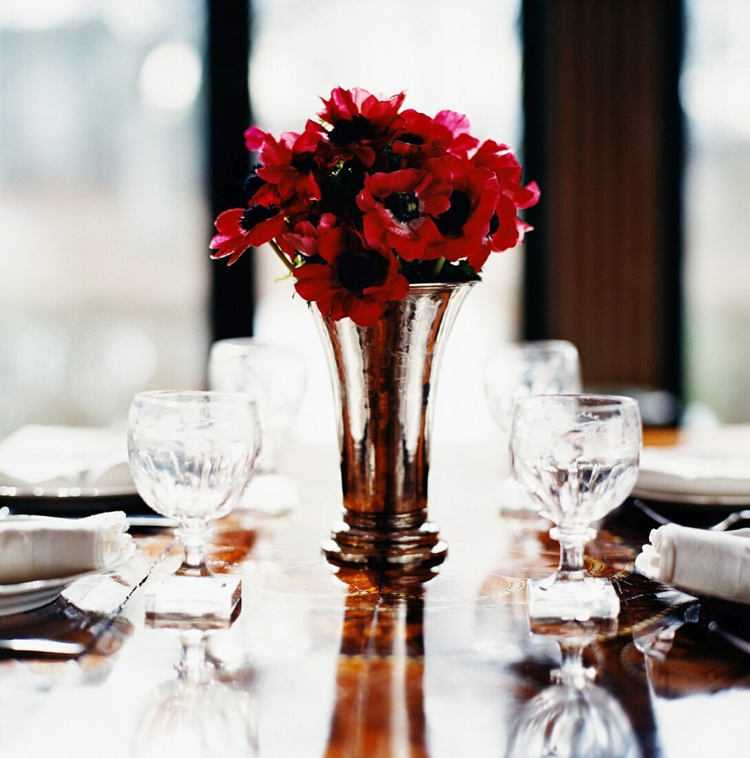 Rote Anemonen in einer Vase auf gedecktem Tisch