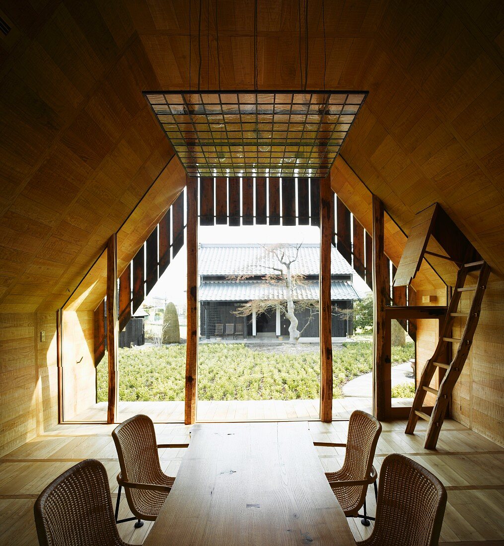 Esstisch aus Holz mit Rattanstühlen im holzverkleideten Wohnraum und Blick auf japanischen Innenhof