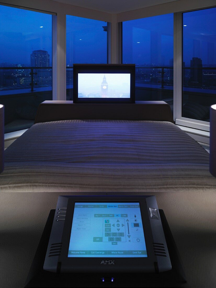 Flachbildfernseher am Bettende eines Doppelbettes vor Panoramafenster mit Blick auf die Stadt bei Nacht