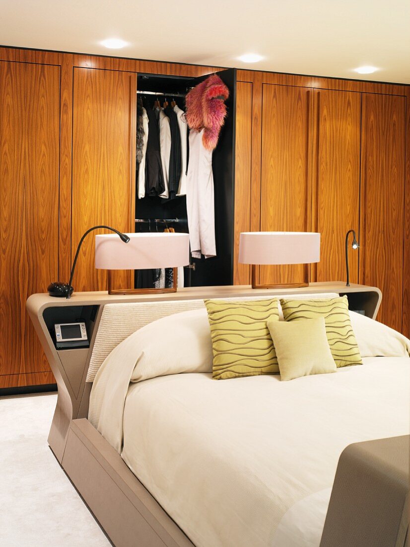 Nachttischleuchten auf Kopfteil des Doppelbetts vor Einbauschrank aus Holz mit geöffneter Tür