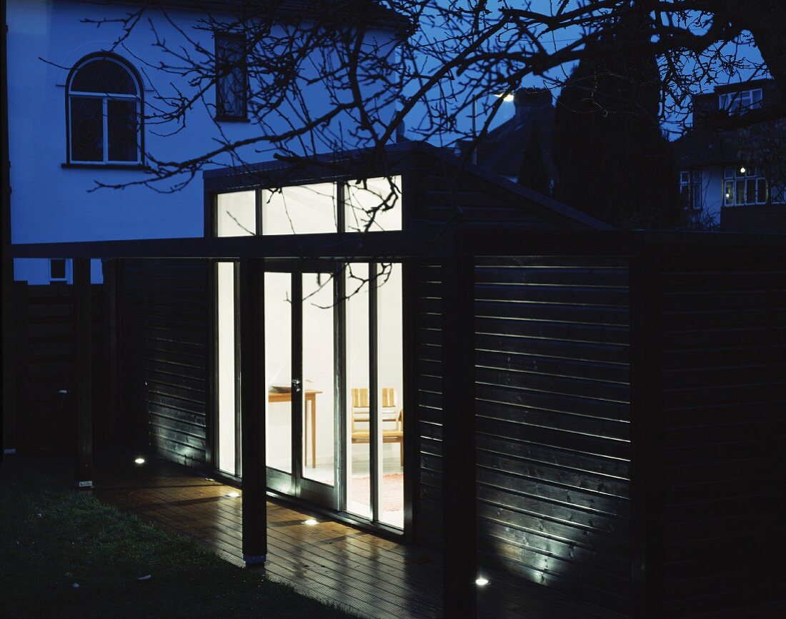 Moderner Anbau aus Holz in Abendstimmung und beleuchteter Innenraum