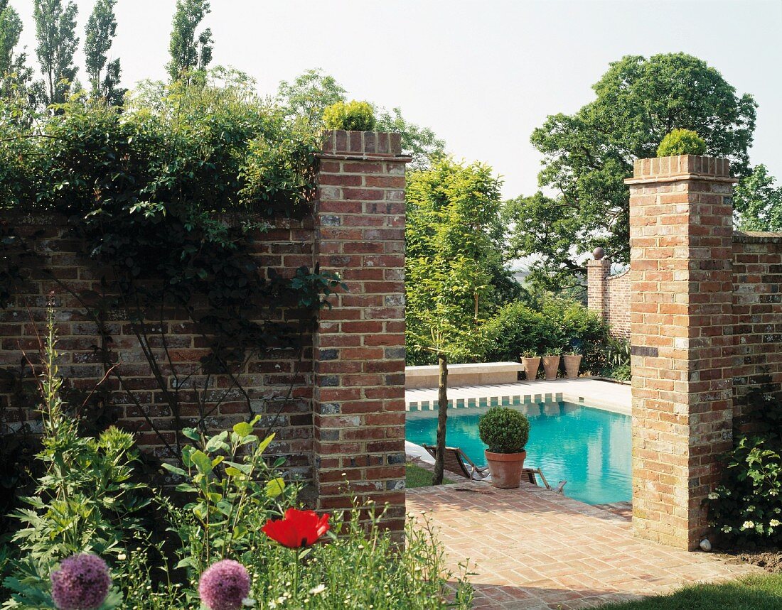 Opening in brick wall with view of pool and trees