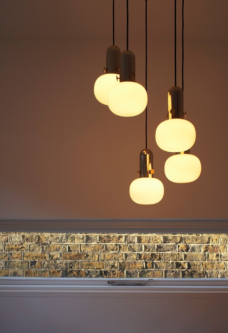 Lit retro light fittings above slit window with view of brick wall