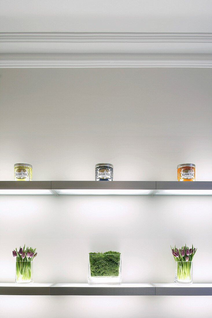 Dekoration von hübschen Lebensmittelgläsern und Blumen auf beleuchteten Glasregalen