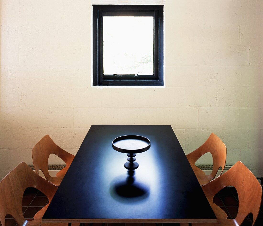 Purist room with perforated wooden shell chairs and ornamental platter on dark table