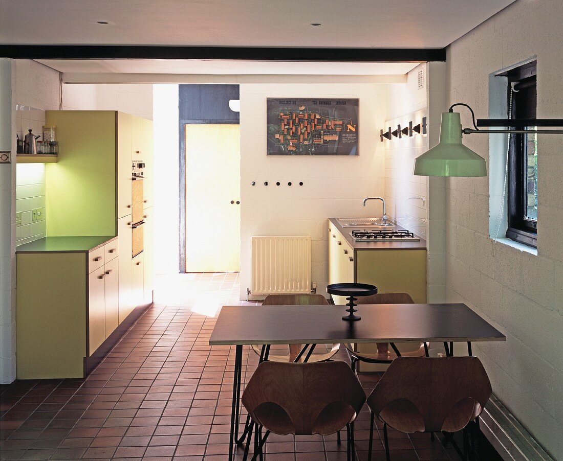 Offene, pastellgelbe Einbauküche mit leichten Essplatzmöbeln und Wandlampe im Industriestil