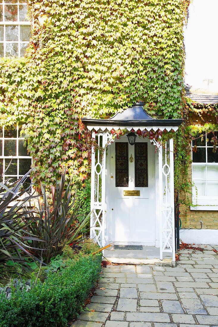 Historische, weiße Haustür mit verziertem Kupferdach unter weinberankter Fassade