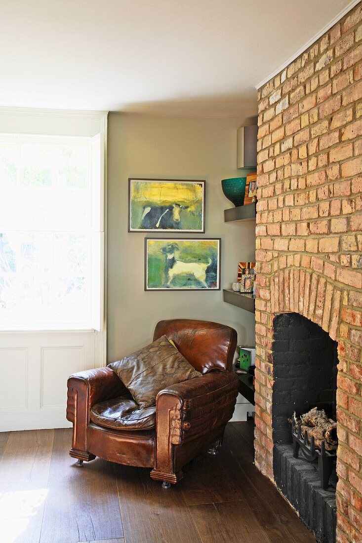 Antique leather armchair next to historic, exposed brick chimney breast