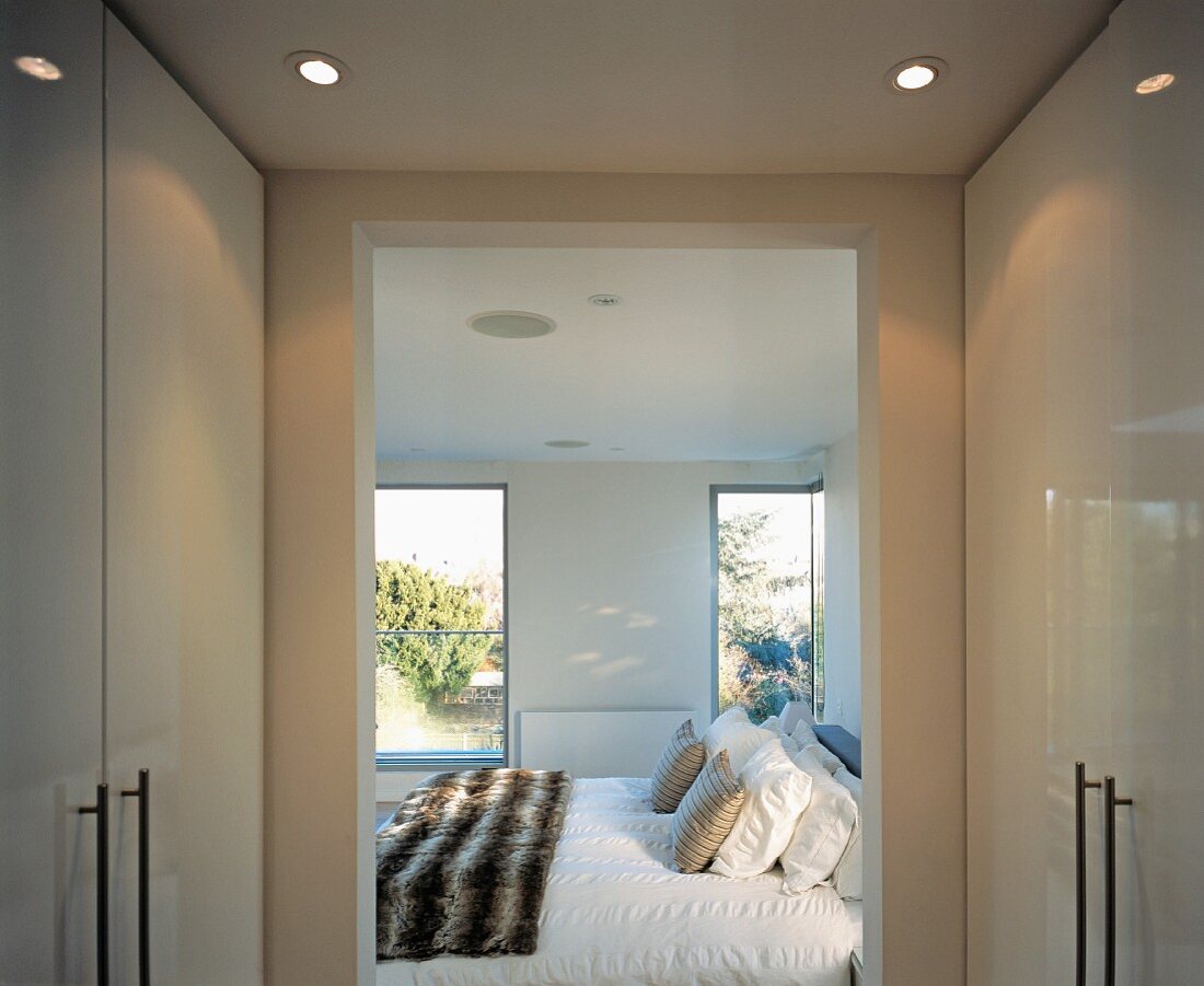 Dressing room with white, glossy fitted wardrobes and open doorway to inviting bedroom