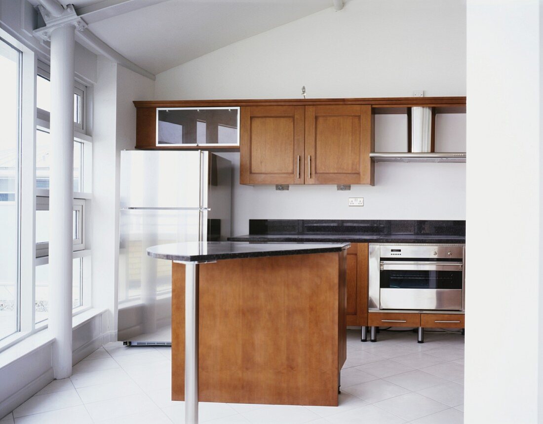 Theke mit schwarzer Granitplatte und Edelstahl-Kühlschrank in moderner Einbauküche mit Holzfronten