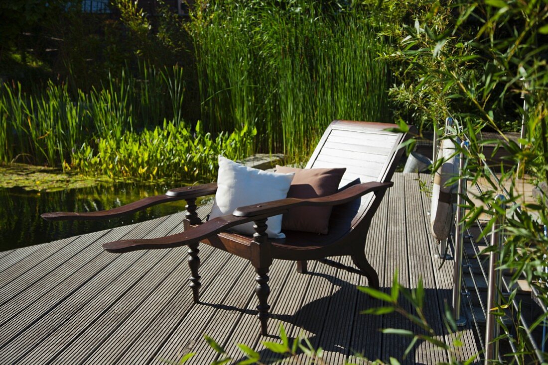 Lounger with cushions next to garden pond