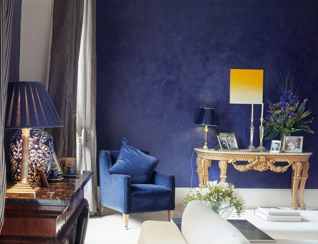 Blue armchair next to small, Rococo table against blue-painted wall