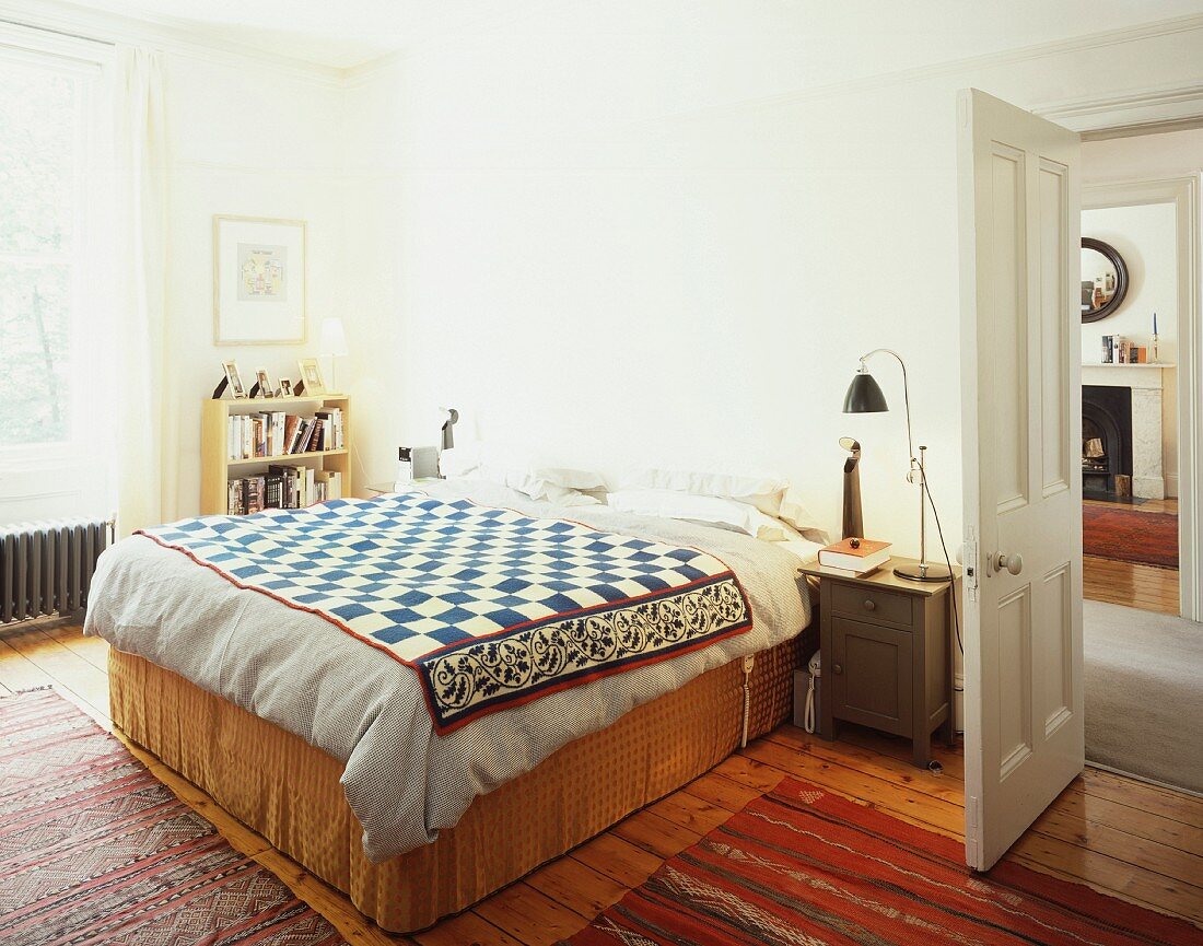 Doppelbett mit Tagesdecke im Ethnostil im Schlafraum und geöffnete Tür