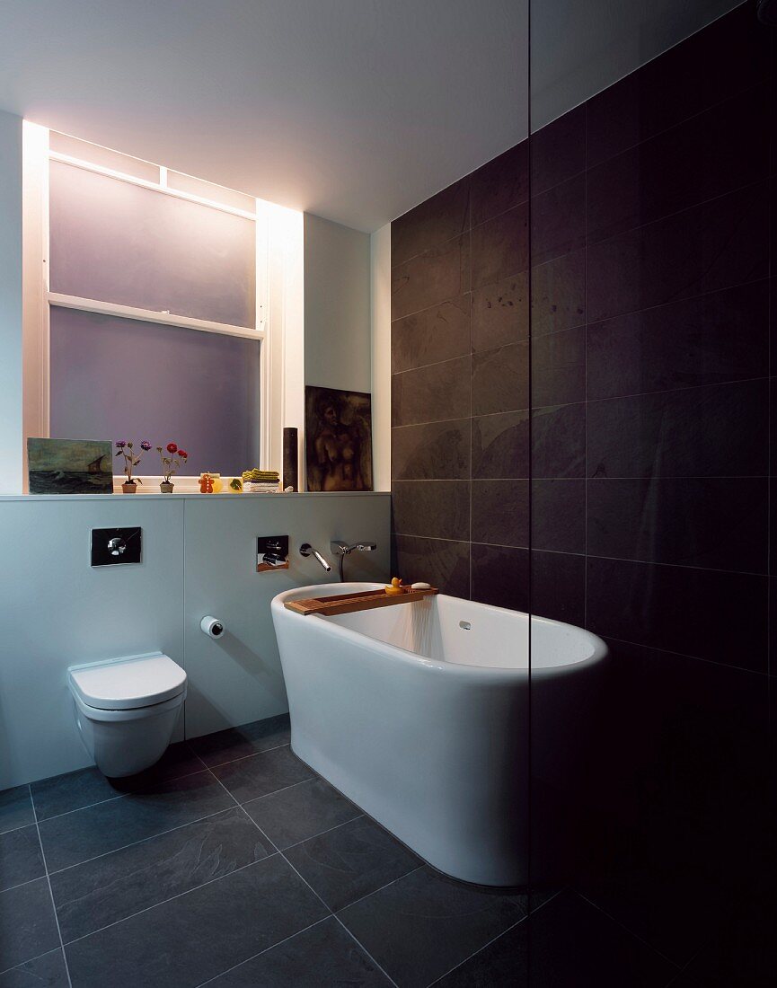 Free-standing bathtub on grey tiled floor in front of dark grey wall