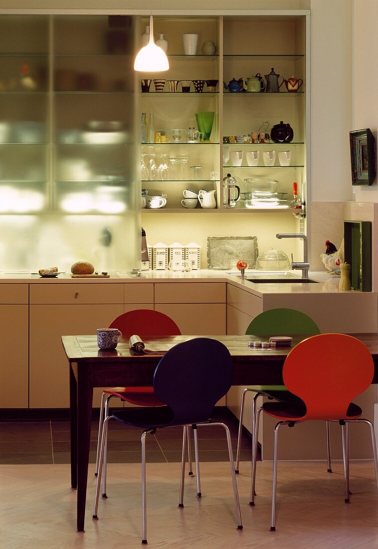 Colourful Bauhaus chairs in dining area in front of half open kitchen cupboard