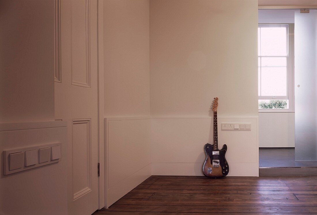 Guitar leaning on wall on floorboards in foyer