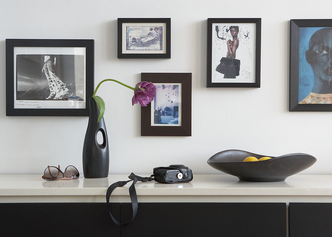 Vase mit Tulpe und schwarze Schale auf Sideboard vor Wand mit gerahmten Photos