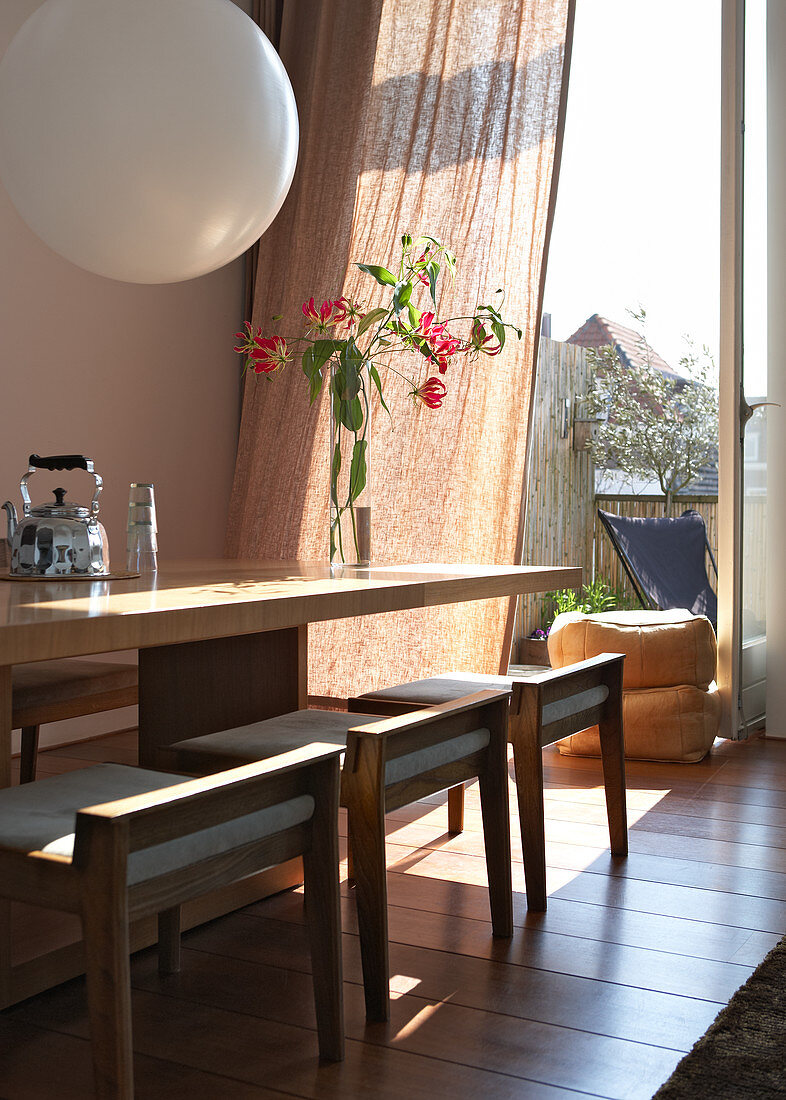 Tisch mit gepolsterten Hockern aus Holz im Designerstil vor offener Balkontür
