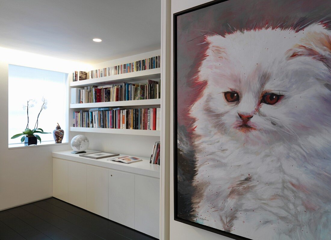 Bild mit Katzenmotiv an Wand im Vorraum und Blick auf Bücherregal über weisses Sideboard