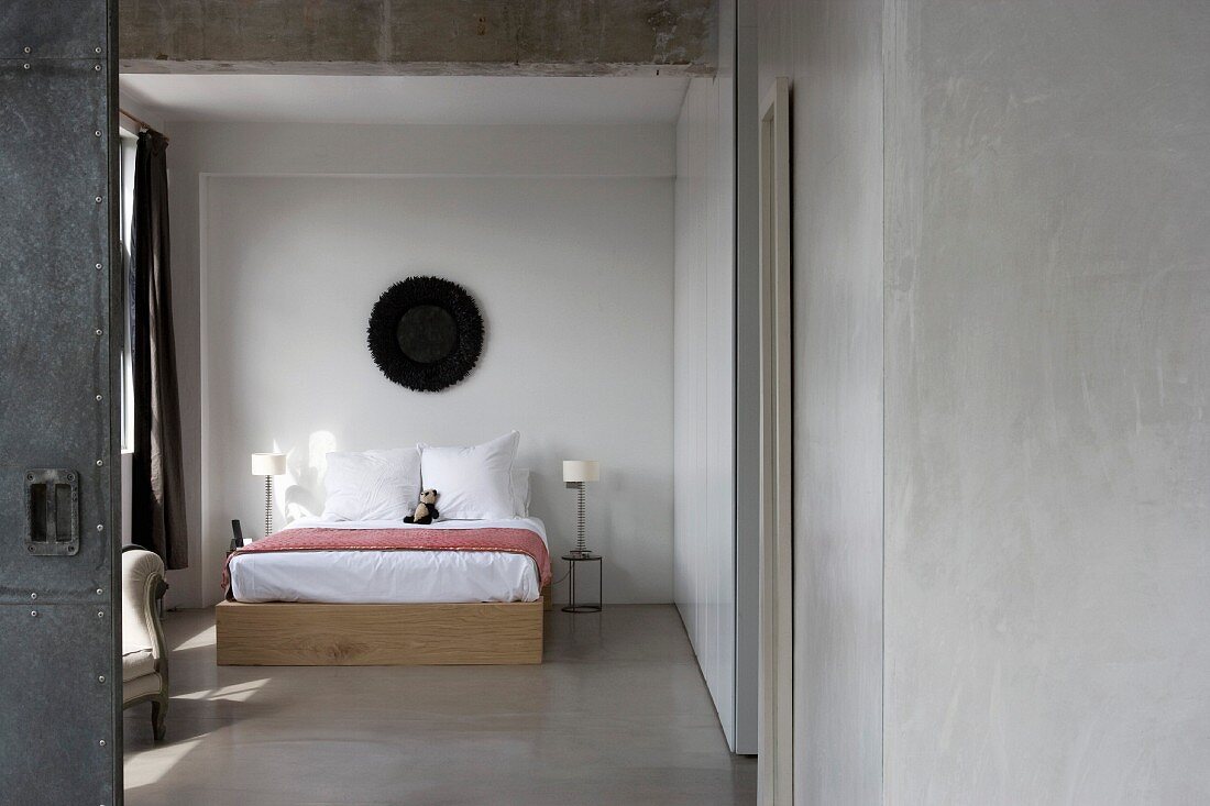 Blick durch offene Tür auf schlichtes Doppelbett im Schlafzimmer mit Estrichboden