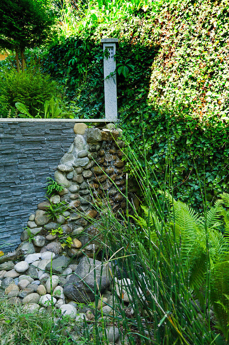Gartenmauer aus Schiefer und Kieselsteinen vor Efeuwand