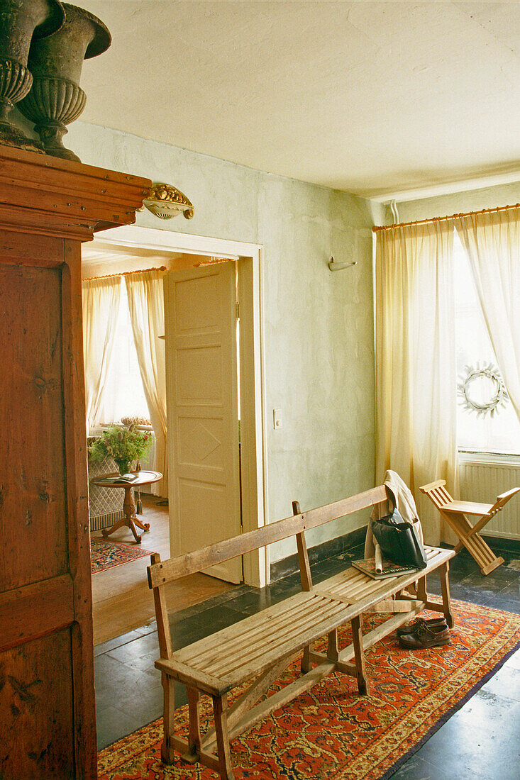 Wooden bench in rustic hallway with carpet and light-colored curtains
