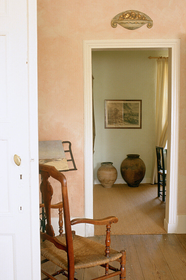 Wooden chair in the foreground with a view of antique vases through the doorway