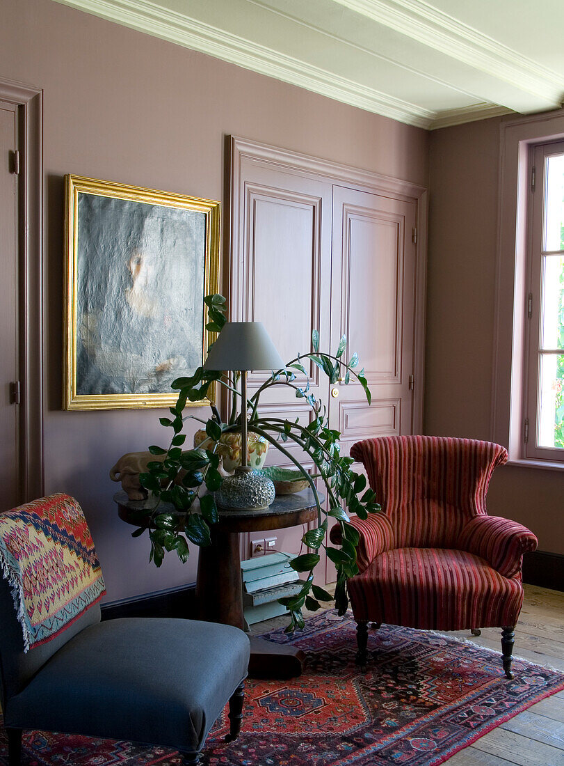 Walls in antique pink, upholstered armchair, table with plant and oriental rug in the living room