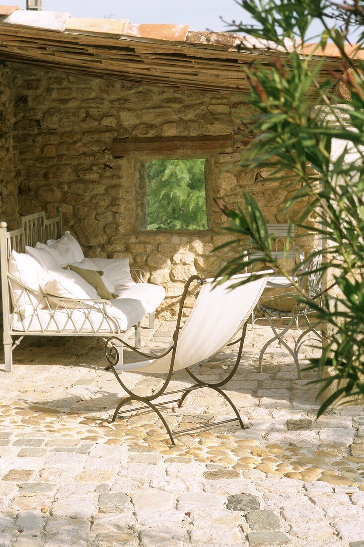 Bench and deckchair on roofed terrace with stone wall
