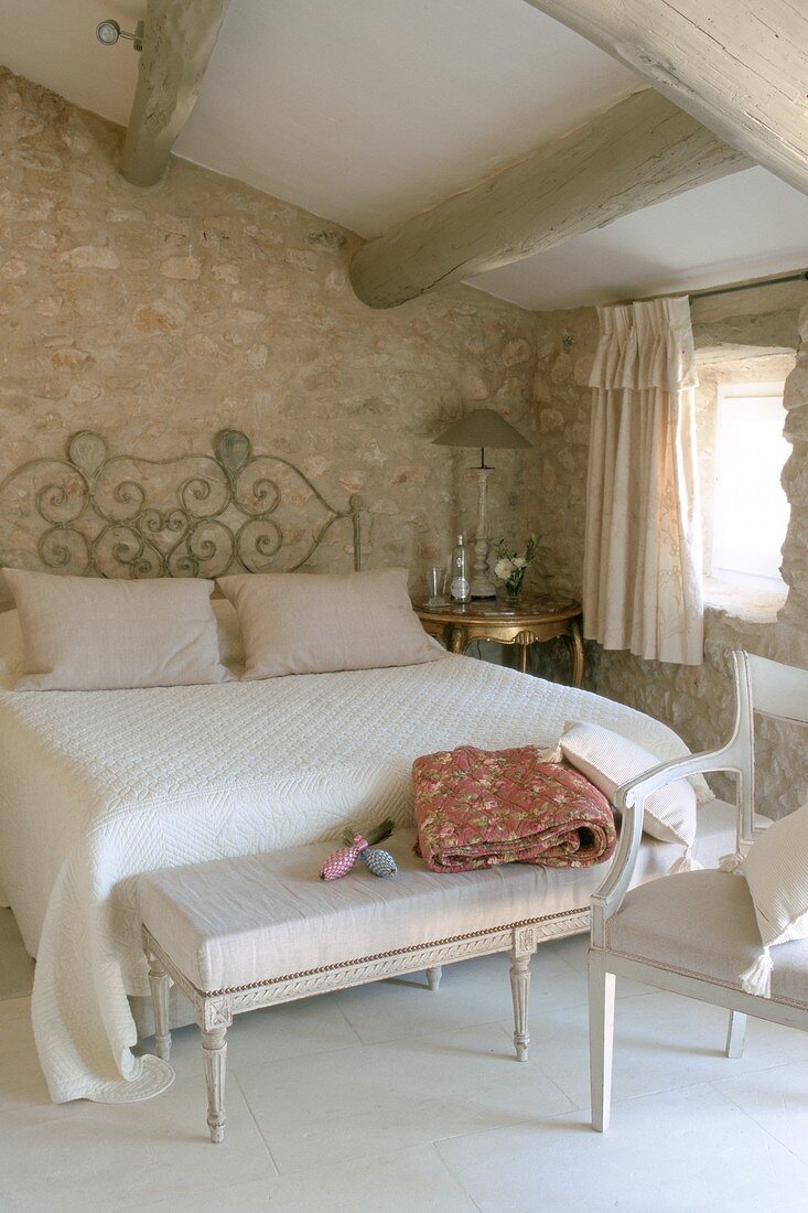 Doppelbett mit Ablagebank in einem Schlafzimmer mit Natursteinwänden unter dem Dach
