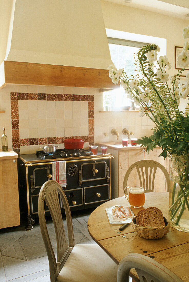 Landhausküche mit Holzstühlen und rustikalem Herd, Blumenschmuck auf dem Tisch