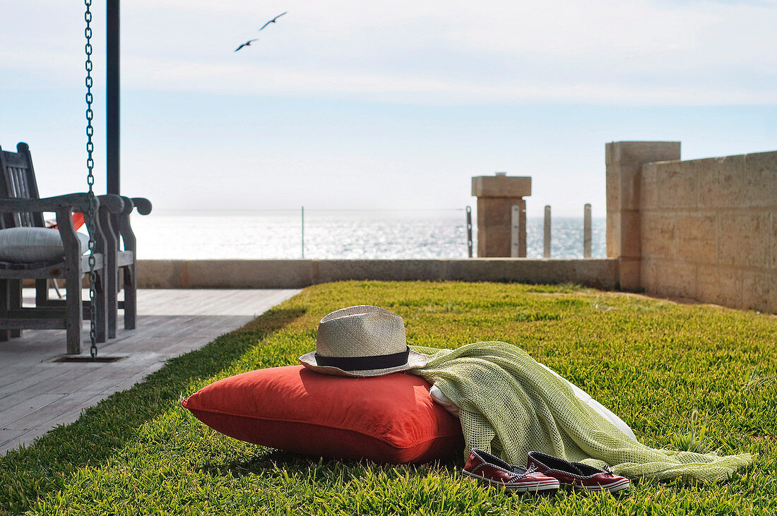 A red pillow and a hat on a lawn with a view of the ocean