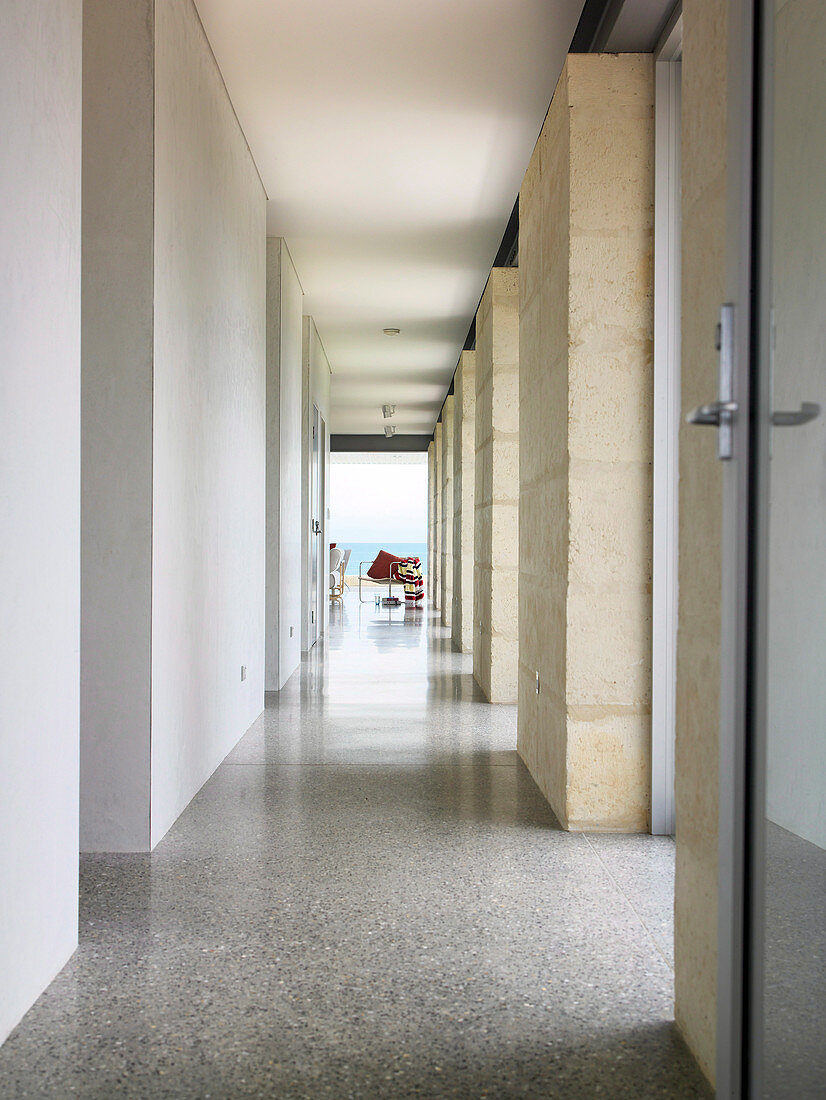 Long, bright hallway with outward opening doors and floor-to-ceiling windows between marble columns