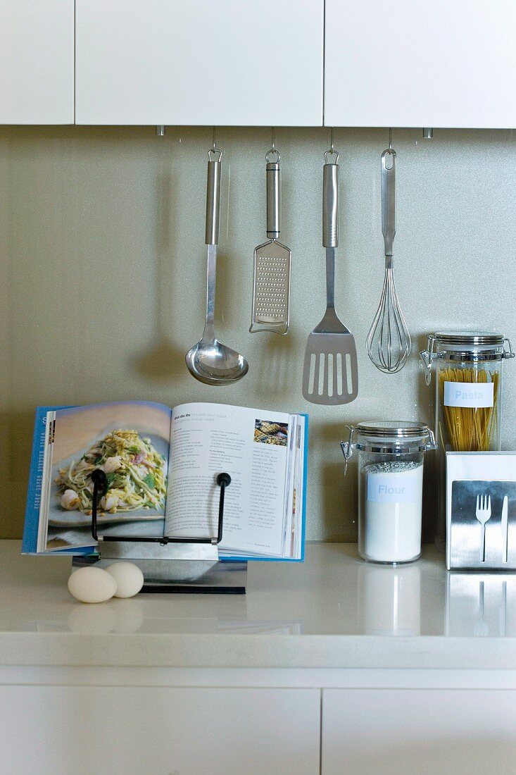 Kitchen utensils and open cookbook on a cookbook stand on a countertop