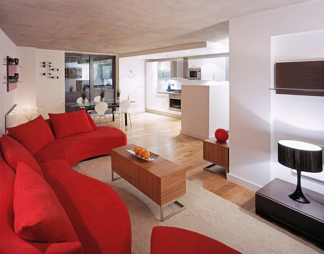 Curved red couch and wooden tables in open-plan living space