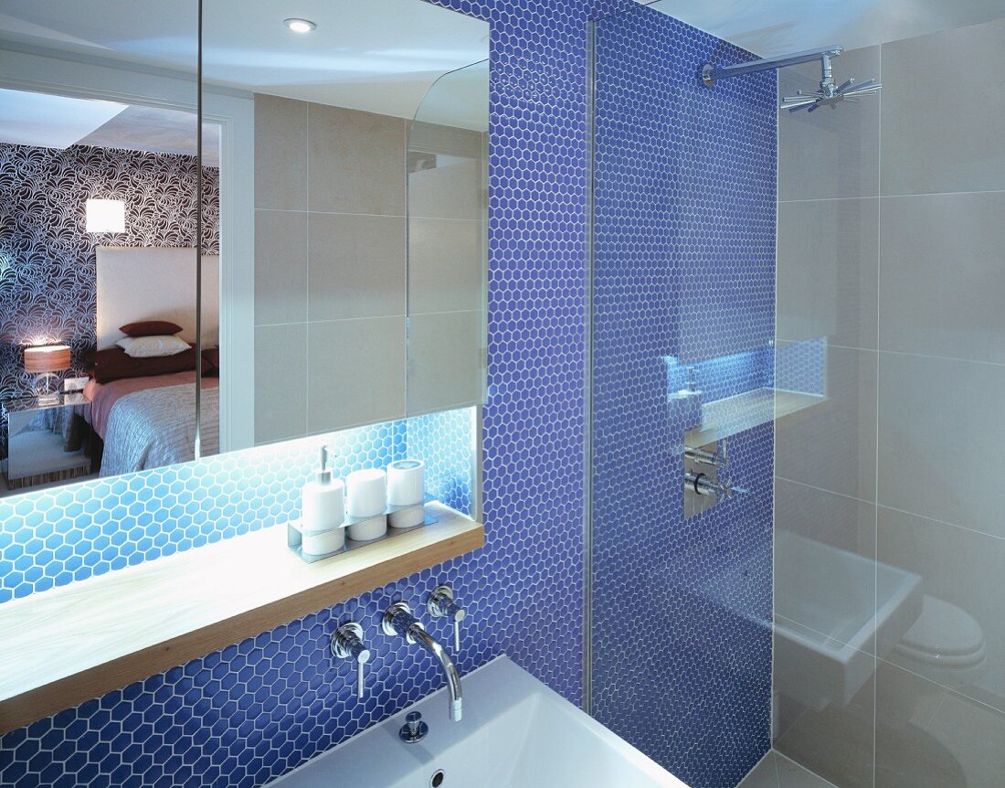 Spiegelschrank mit indirekter Beleuchtung und Dusche vor blauer Mosaikfliesenwand