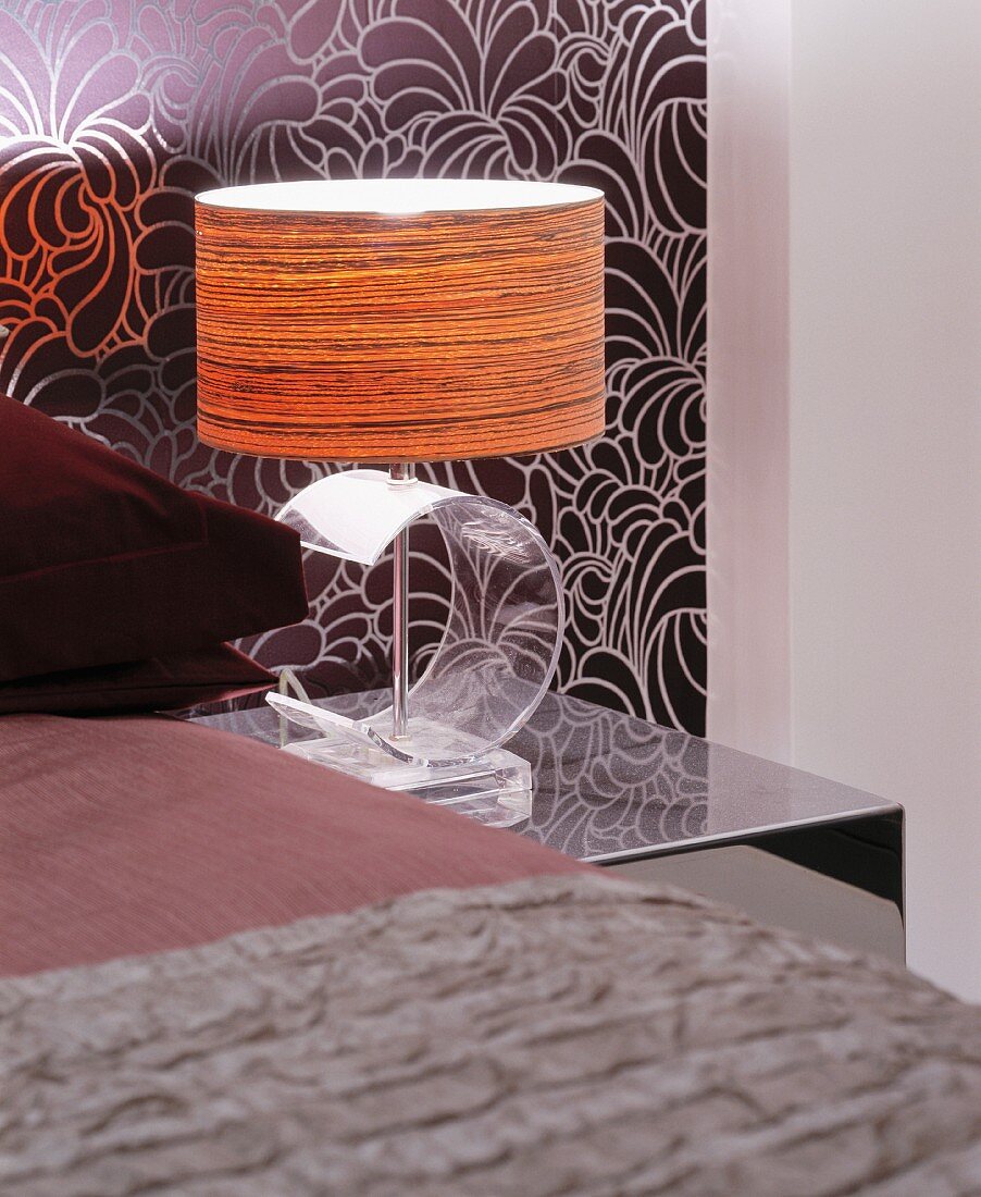 Nachttischlampe mit Fuß aus transparentem Acrylglas vor gemusterter Tapete an Wand