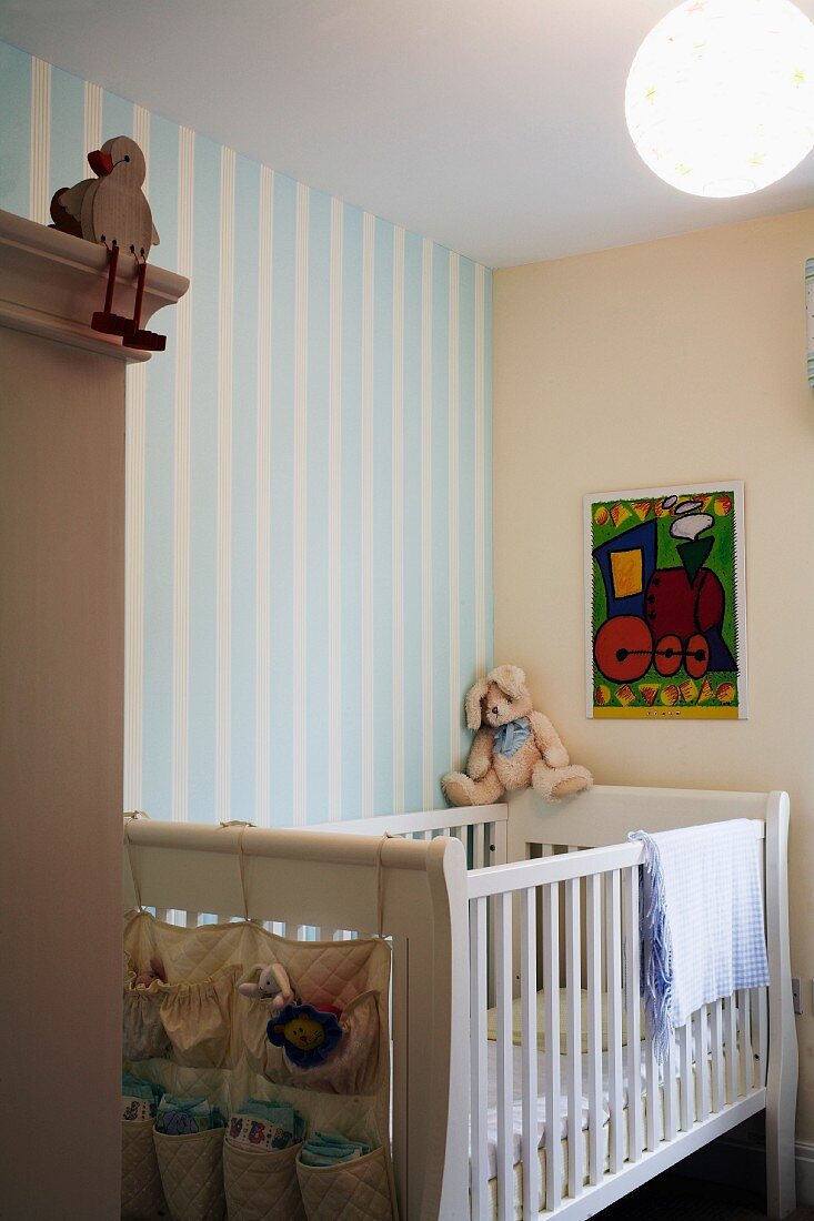 Kinderbett mit weiss lackierten Gitterstäben vor Wand mit Tapete