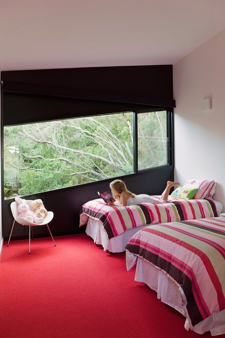 Mädchen liest gemütlich auf einem Einzelbett mit gestreifter Bettwäsche in Designer Schlafzimmer