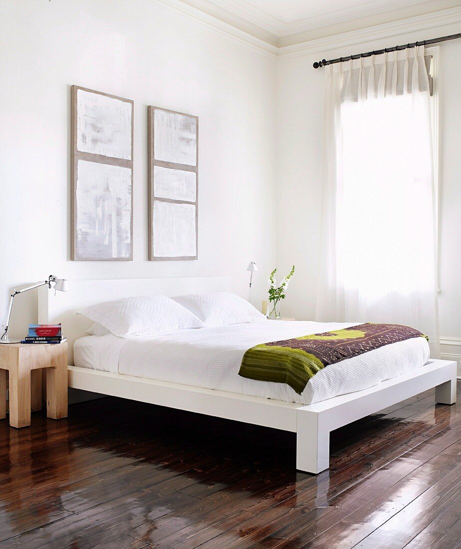 Corner of modern bedroom with modern double bed on glossy floorboards