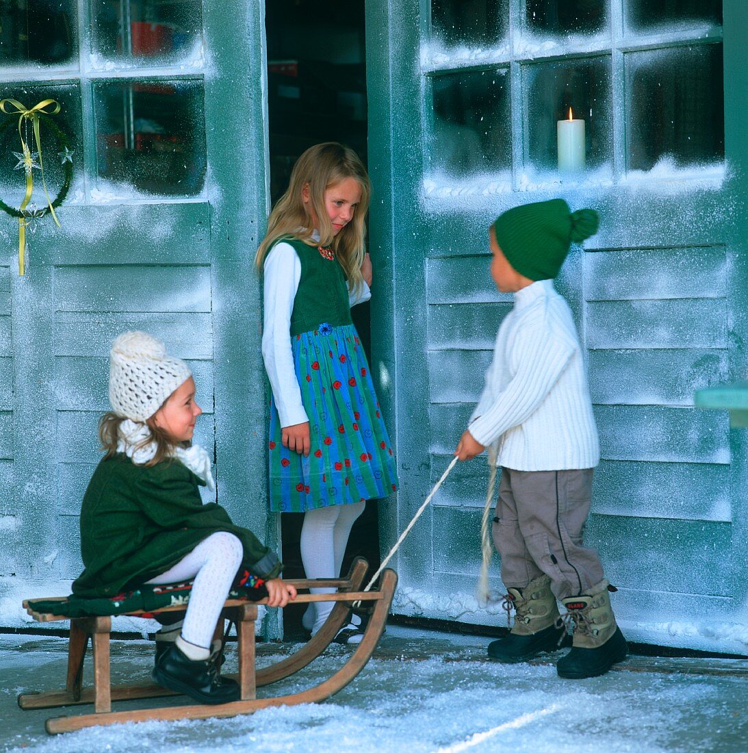 Three children with sledge in front of house