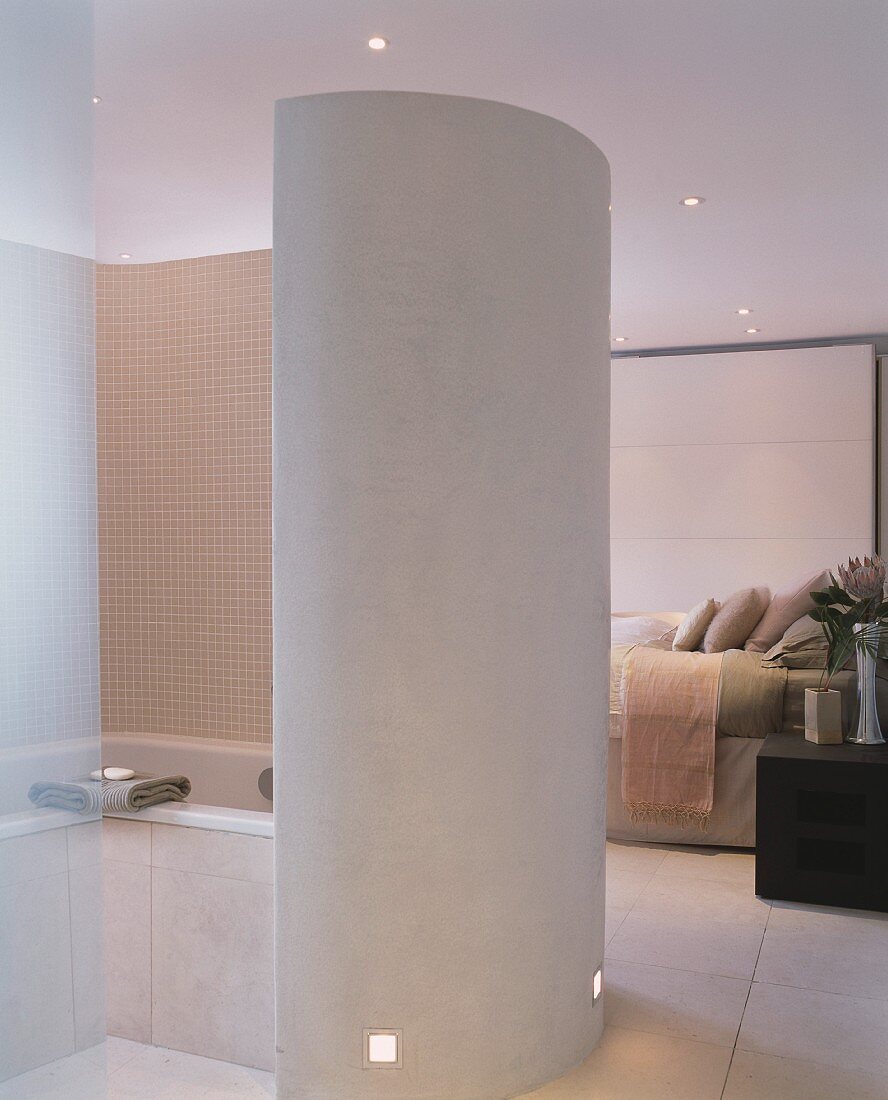 Curved partition around bathtub in open-plan, designer bedroom
