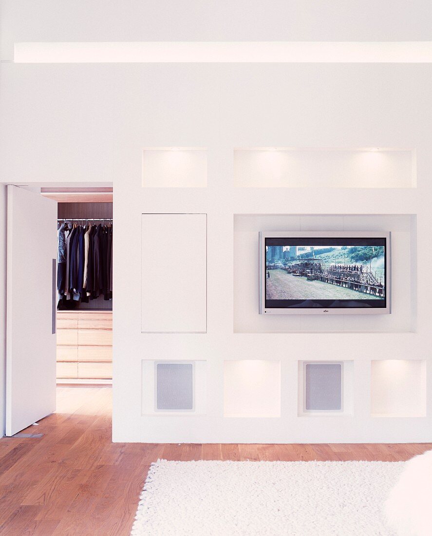 Modern bedroom with flat-screen TV integrated into wall and open door leading to dressing room