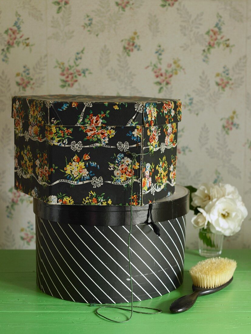 Two hatboxes on table in front of floral wallpaper