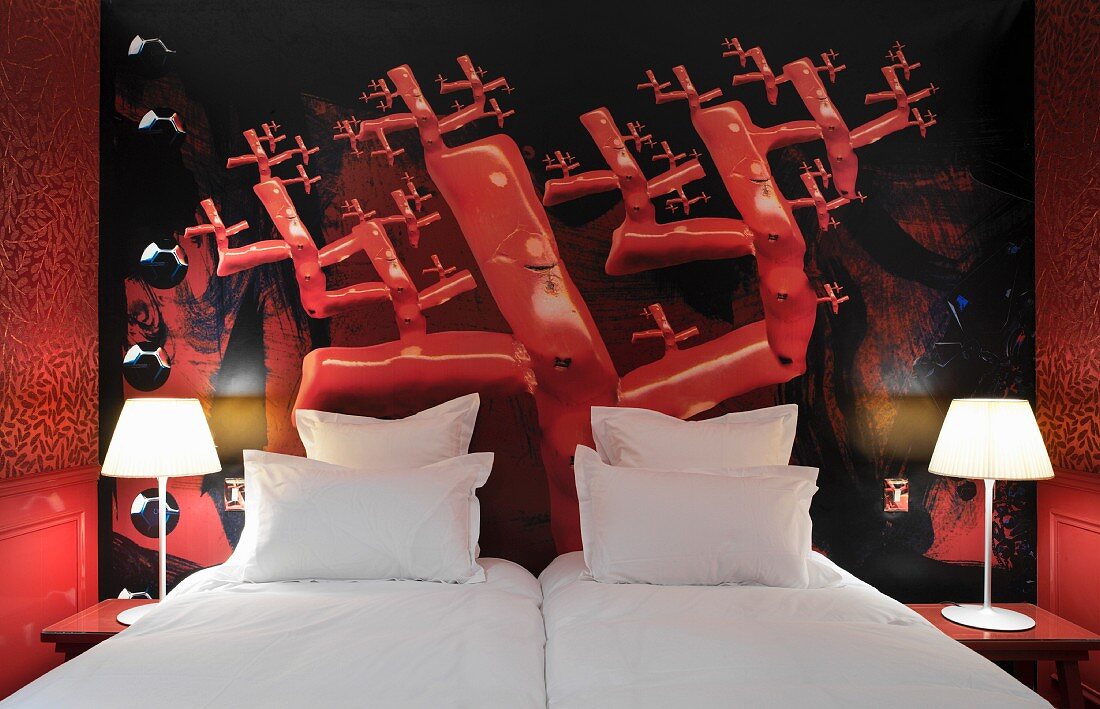 Bright red hotel room with surreal mural motif behind snow-white pillows and lit bedside lamps