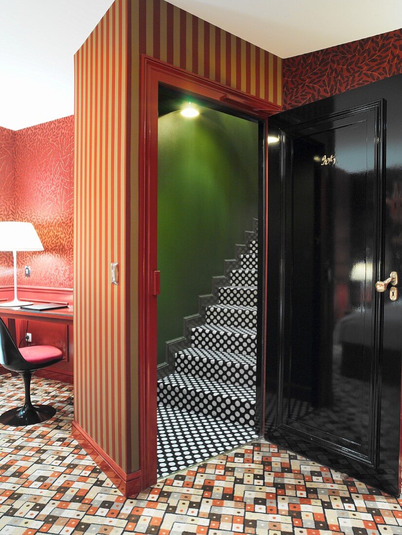 Wild mix of patterns on carpet, wallpaper and stair carpet contrasting with black-lacquer door element and retro chair