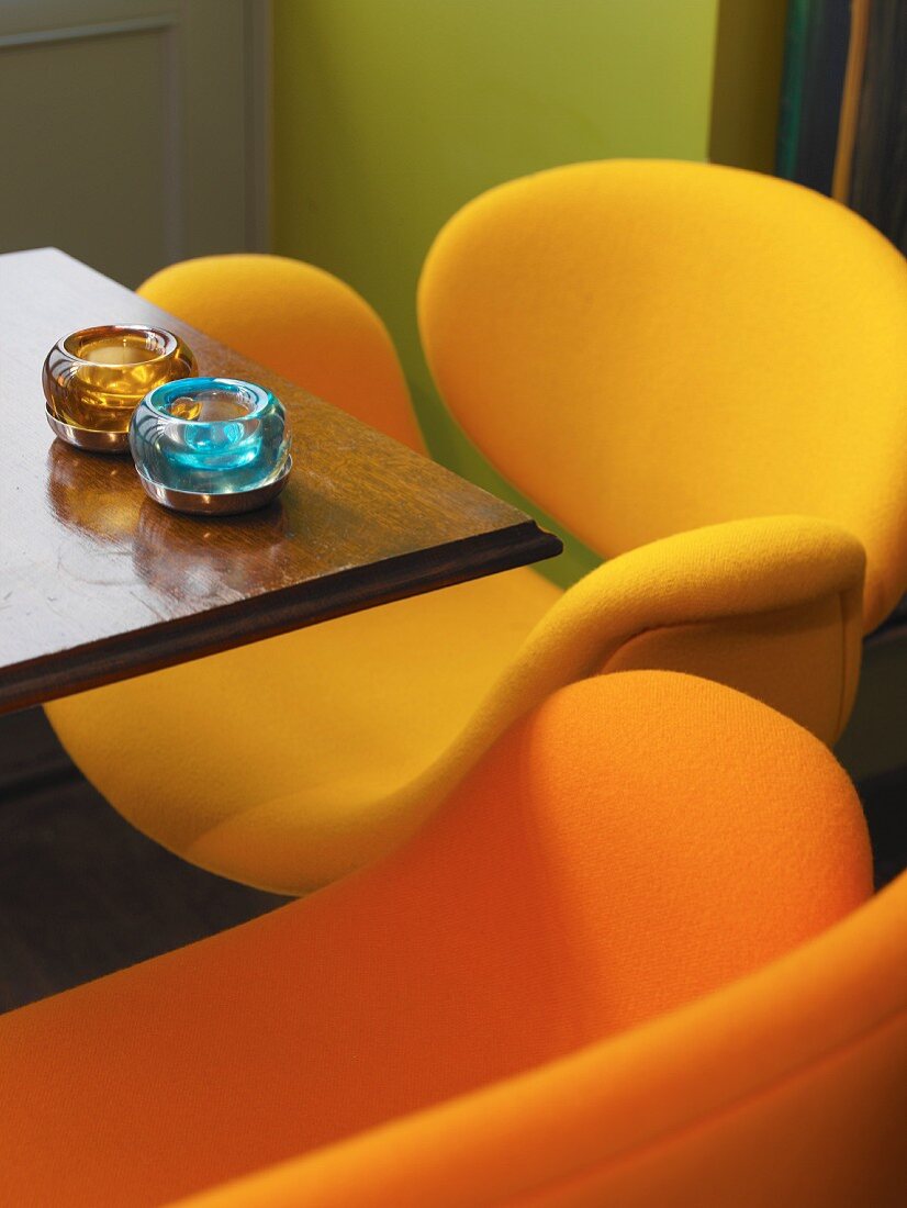 Kleiner Tisch in einer Bar mit knallorange und gelben Schalensesseln im Retrostil