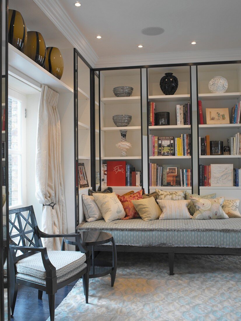 Classic, modern seating corner with vases and books in fitted shelving